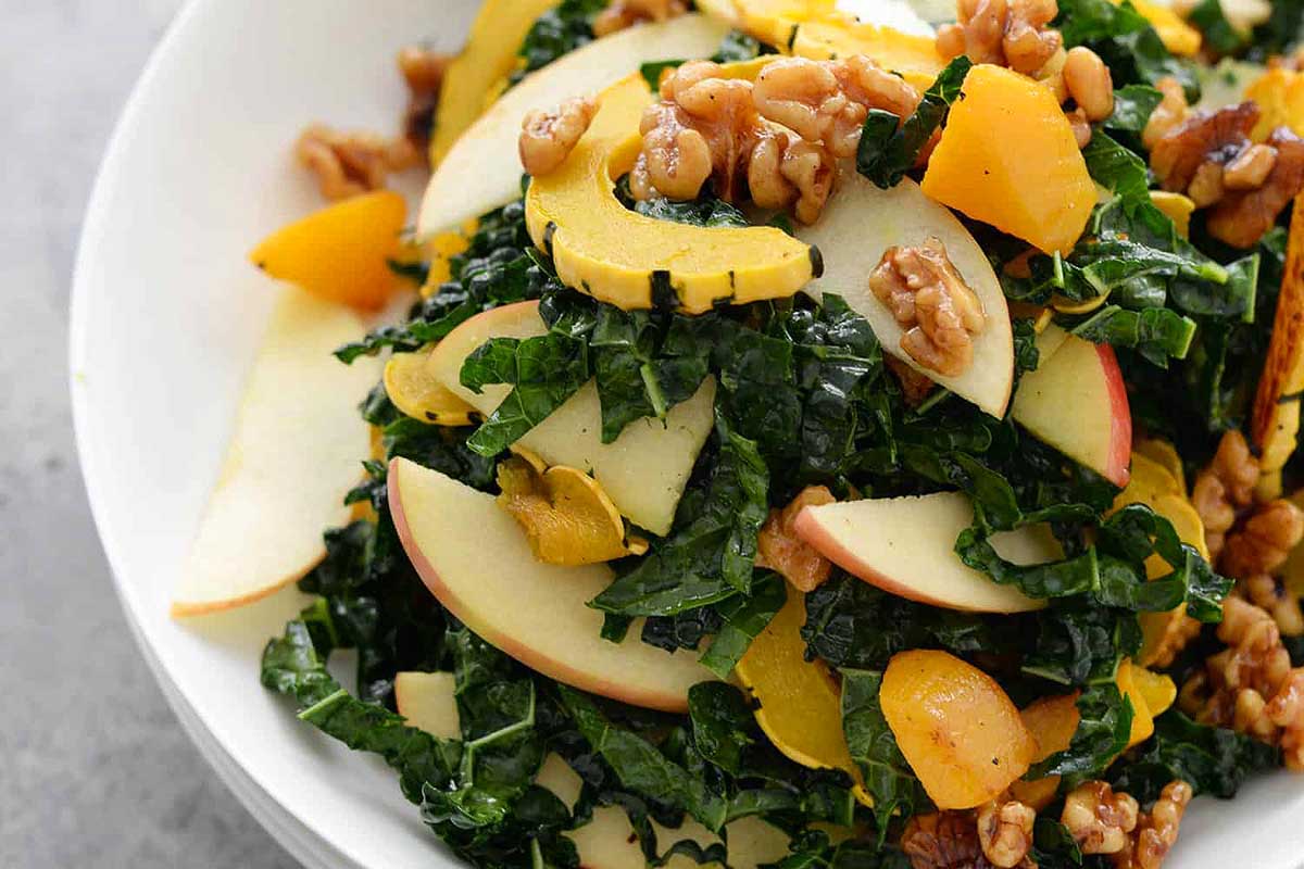A bowl of kale salad with apples and walnuts.