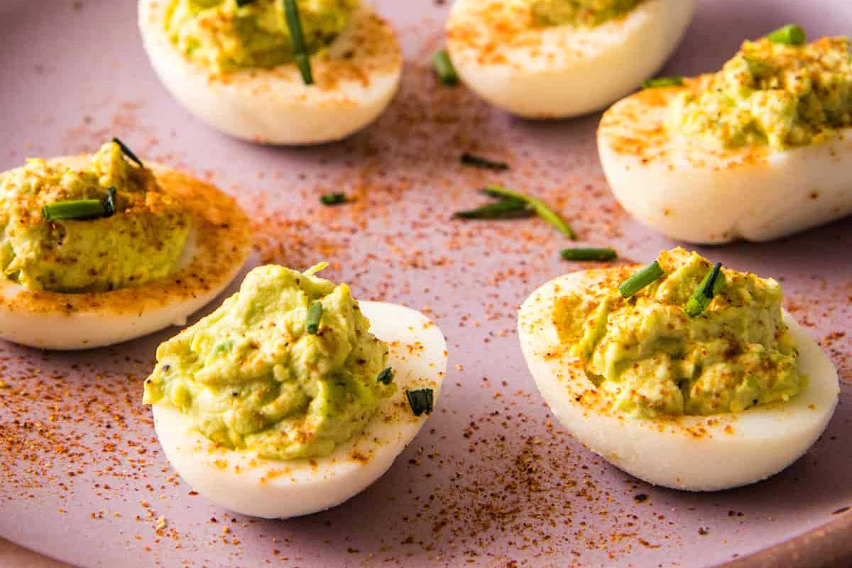 Deviled eggs with guacamole and chives on a purple plate.