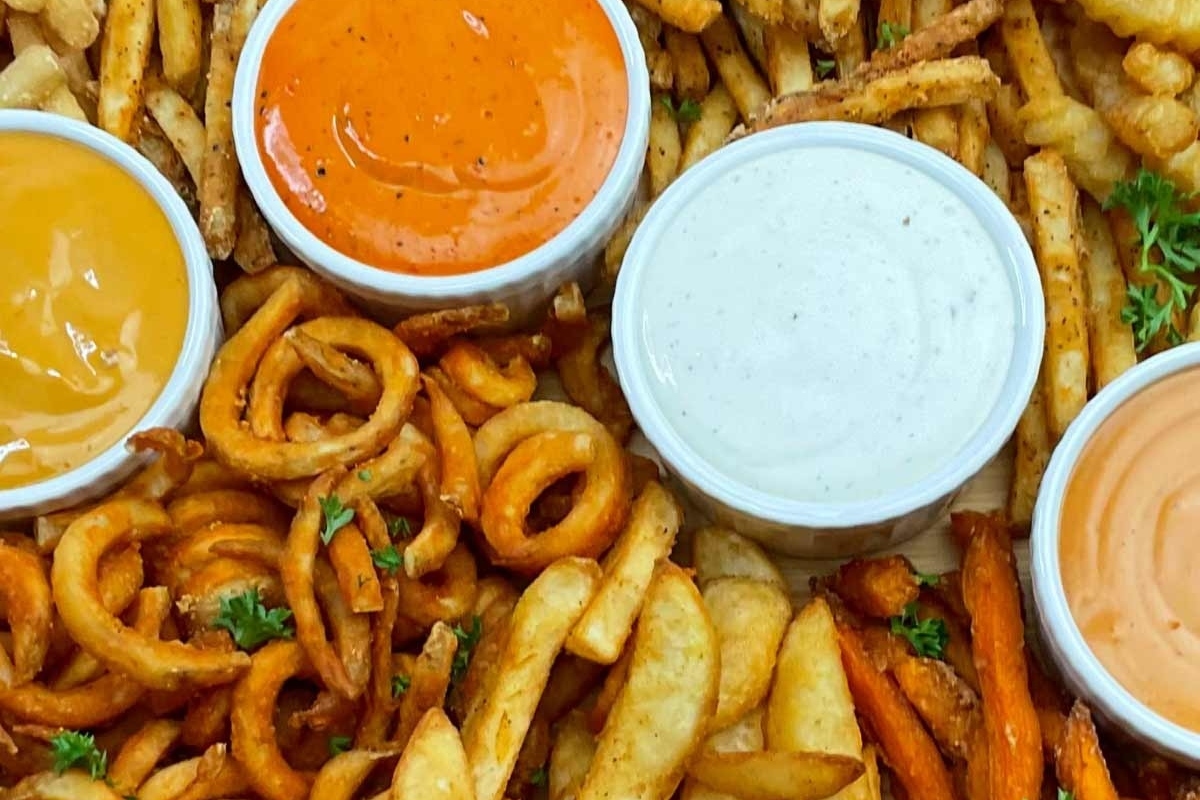 Delicious Fry Recipes featuring a tray of french fries, onion rings, and dips.