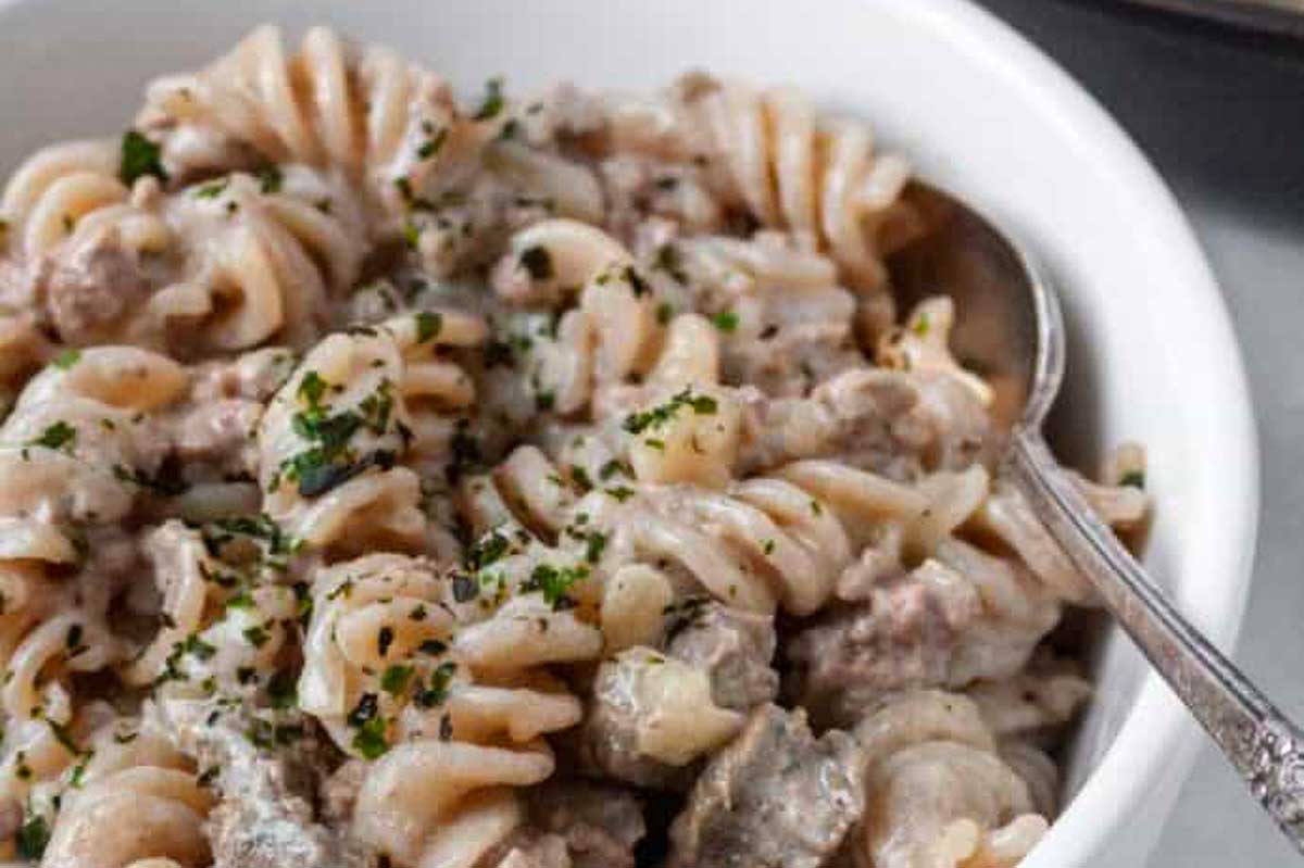 A white bowl with pasta and meat in it.