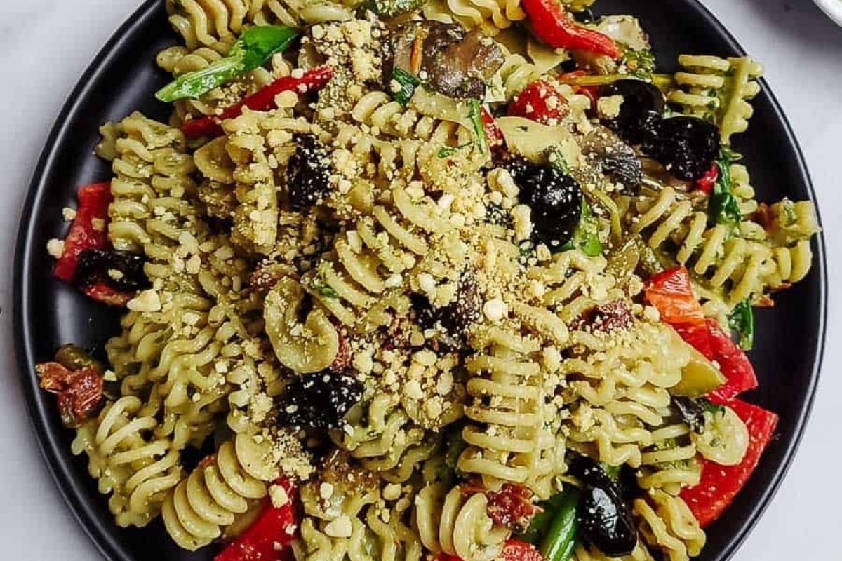 A plate of pasta with pesto and olives on it.