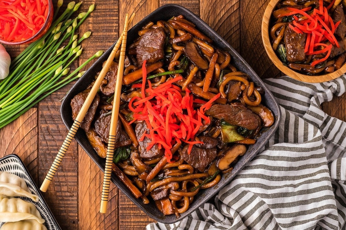 Asian beef stir fry on a wooden table with chopsticks.