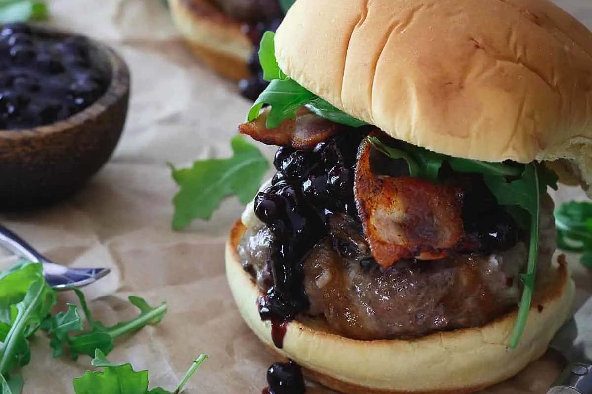 A burger with blueberries and bacon on top.