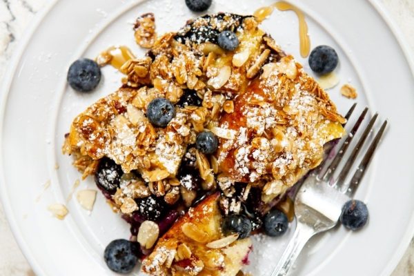 A plate of blueberry french toast with granola and blueberries.