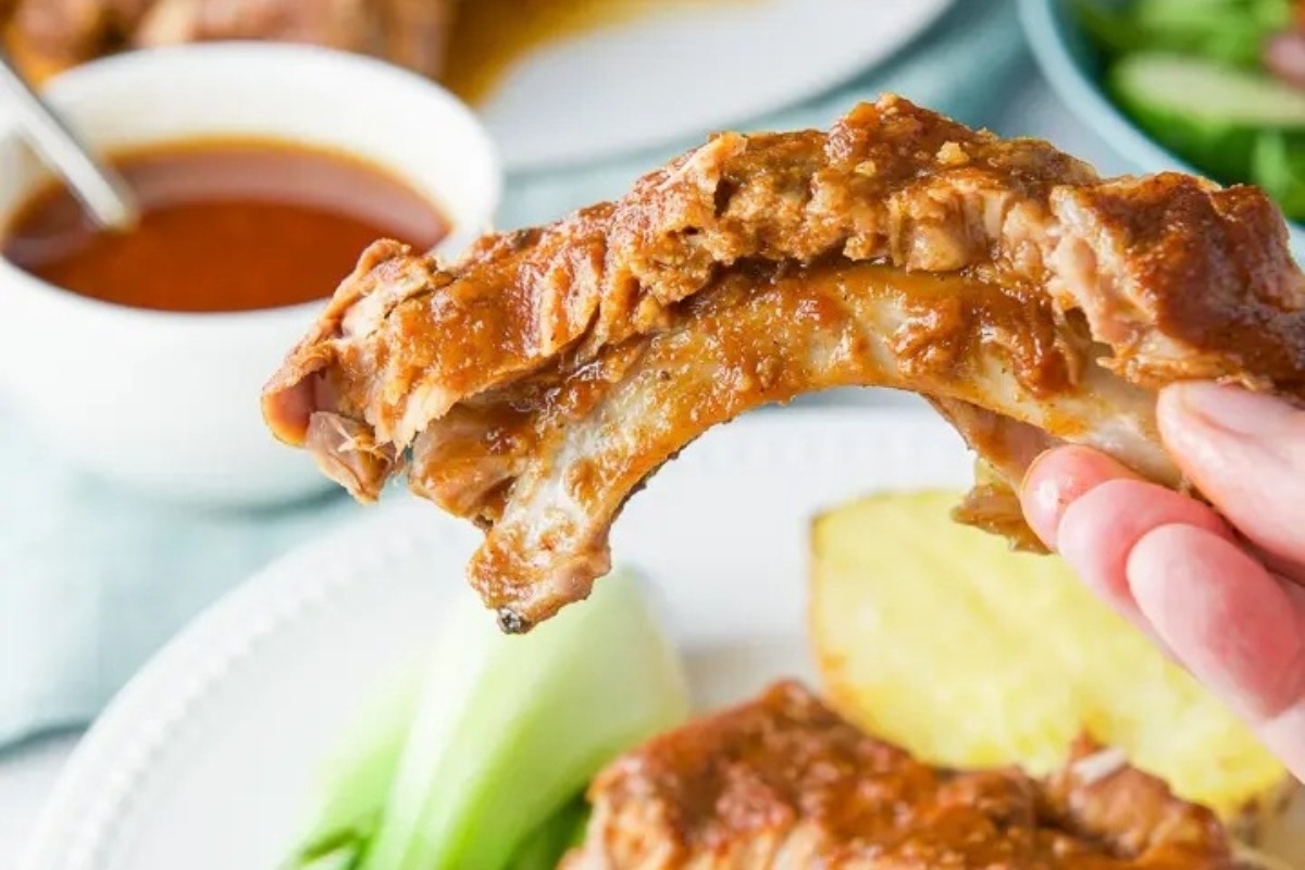 A hand is holding a piece of ribs on a plate, showcasing mouthwatering BBQ recipes.