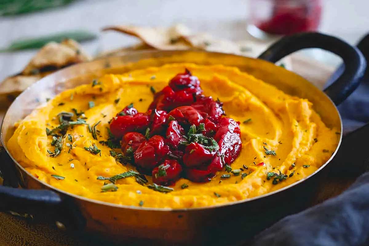 A bowl of hummus with cranberries and herbs.