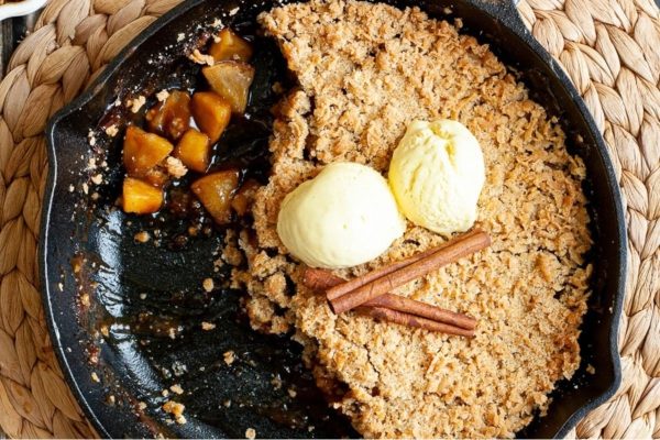 Apple crisp in a skillet with ice cream and cinnamon.
