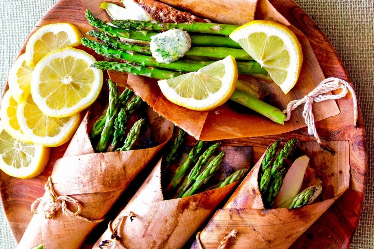 Salmon wrapped in paper with lemon wedges on a wooden plate.
