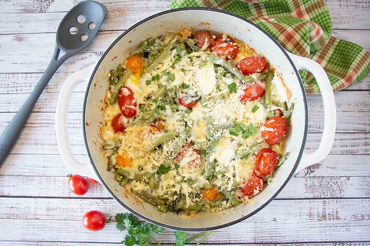 Cheesy asparagus and tomato casserole, a delightful blend of flavors, is served on a rustic wooden table.