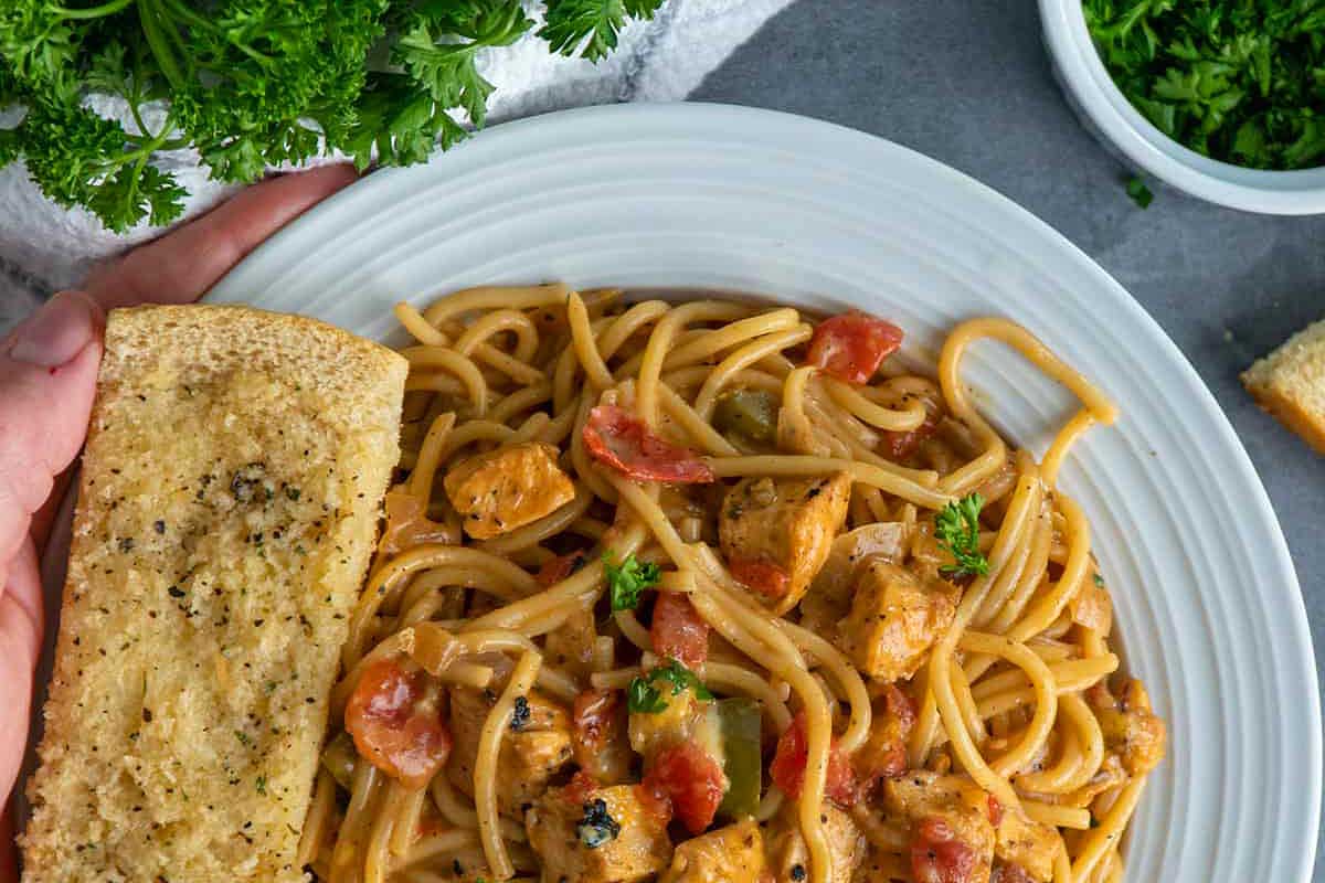 A hand holding a plate of spaghetti with chicken and parmesan.