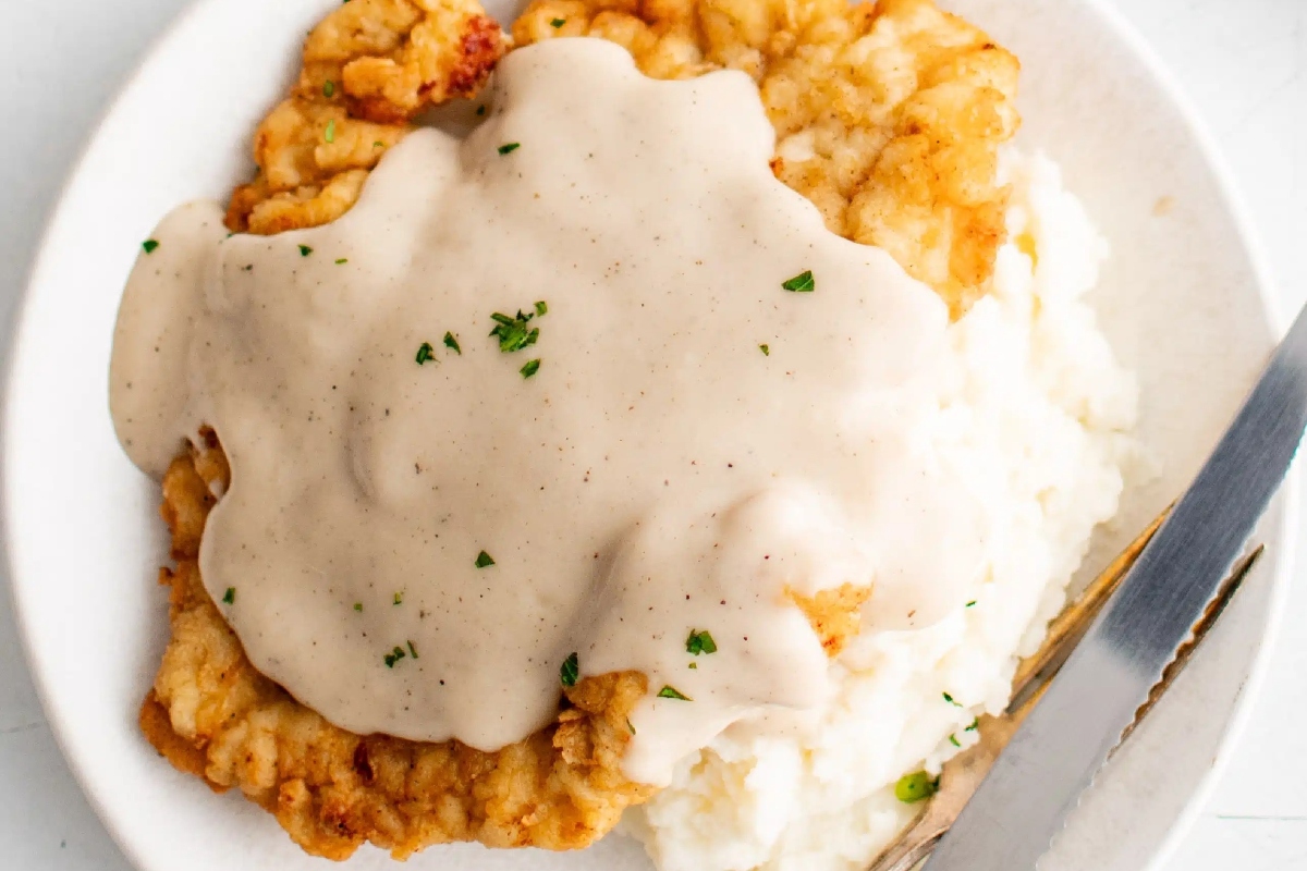 Country-style fried chicken with gravy and mashed potatoes on a white plate.