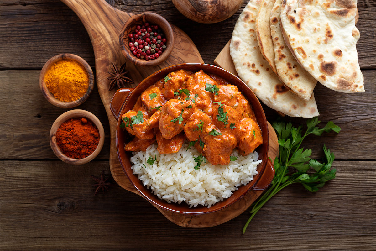 Chicken tikka masala spicy curry meat food in a clay plate with rice and naan bread on wooden background.