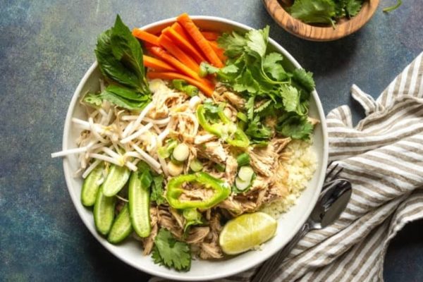 A bowl of thai chicken salad with carrots and cucumbers.