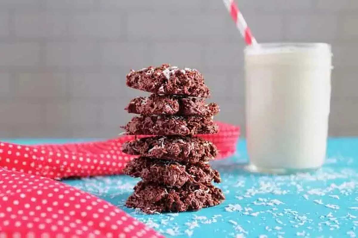 A stack of chocolate coconut cookies next to a glass of milk.
