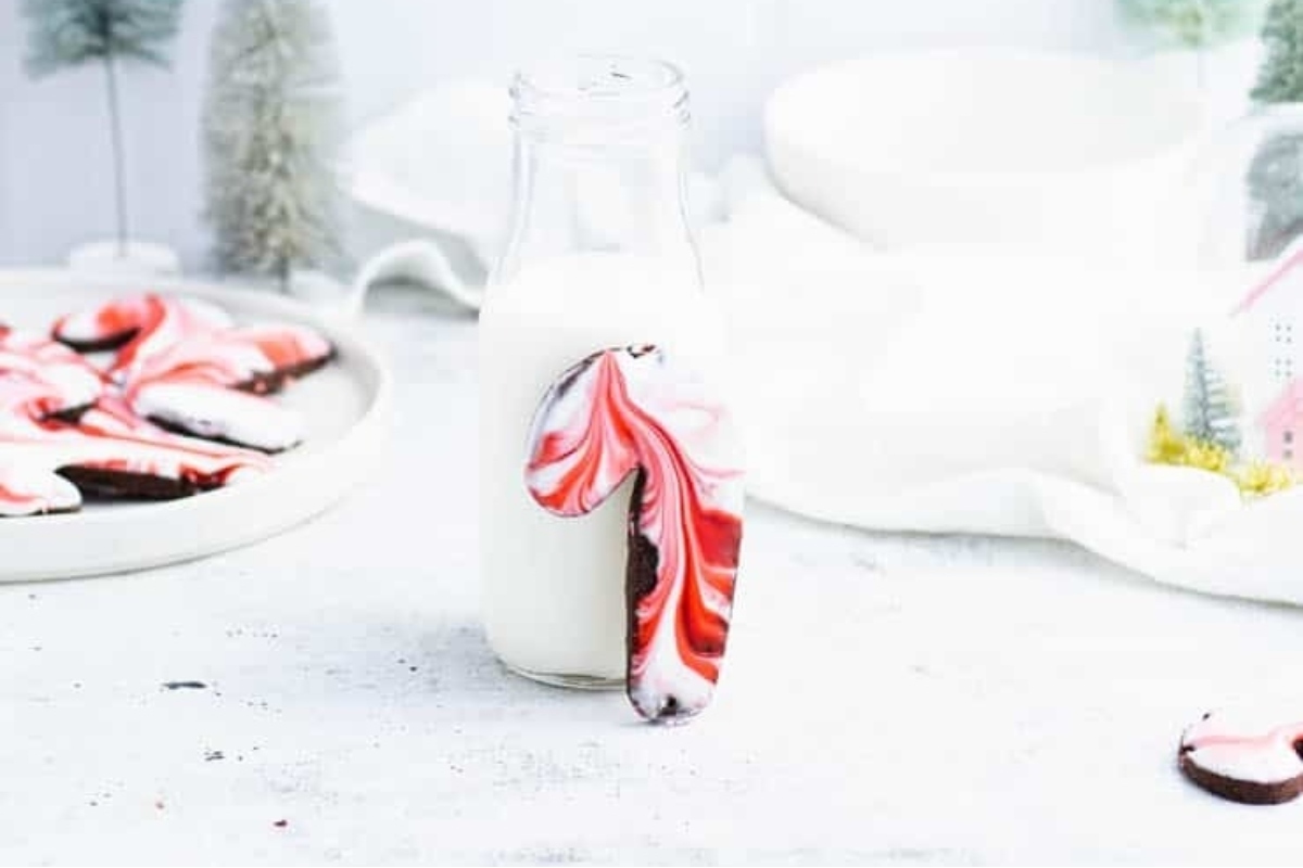 A plate of cookies decorated with candy canes sits next to a glass of milk.