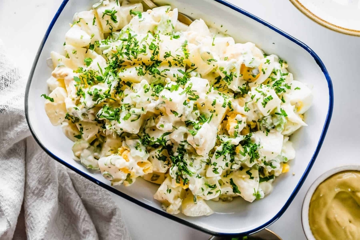 A bowl of potato salad with mustard and parsley.