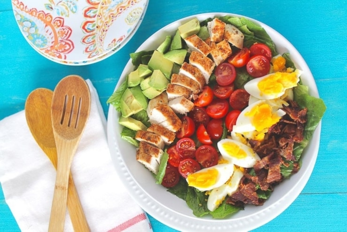 A salad with chicken, avocado, tomatoes and hard boiled eggs.