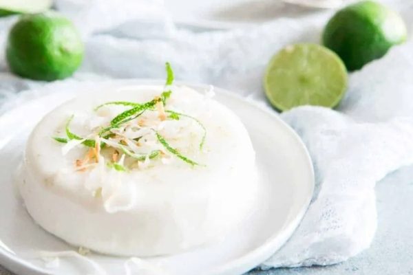 A coconut dessert on a white plate with limes on it.