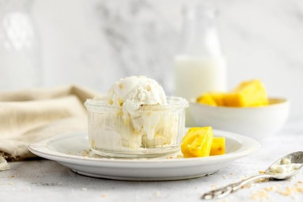 A coconut bowl filled with mango ice cream on a white plate.