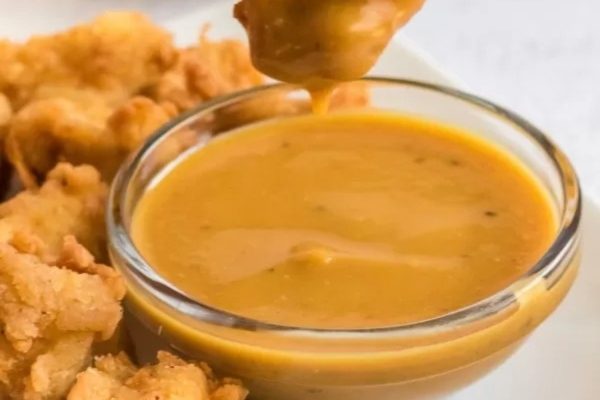A delicious sauce being poured over a bowl of crispy fried chicken.