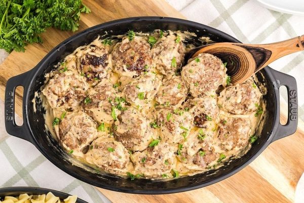 Swedish meatballs in a skillet with pasta and parsley.