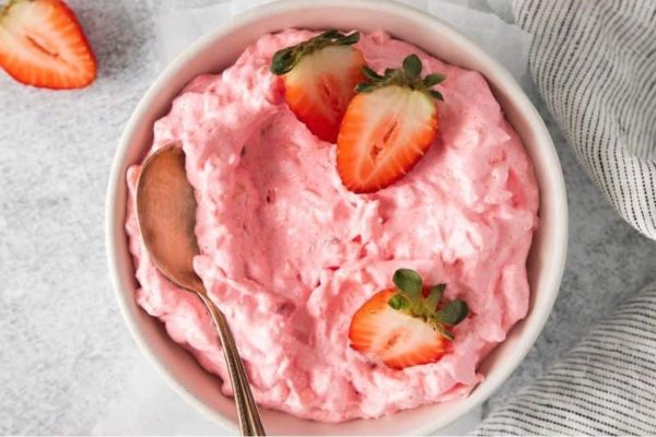Strawberry ice cream served in a white bowl with a spoon.