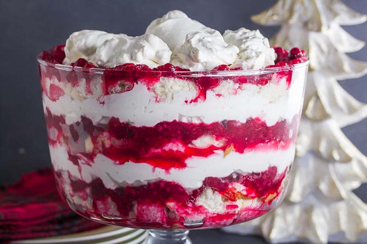 A Christmas trifle in a glass bowl with whipped cream and red raspberries.