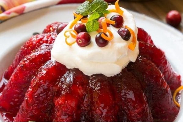 A plate of cranberry pudding with whipped cream on top, a delicious dessert recipe perfect for the holiday season.