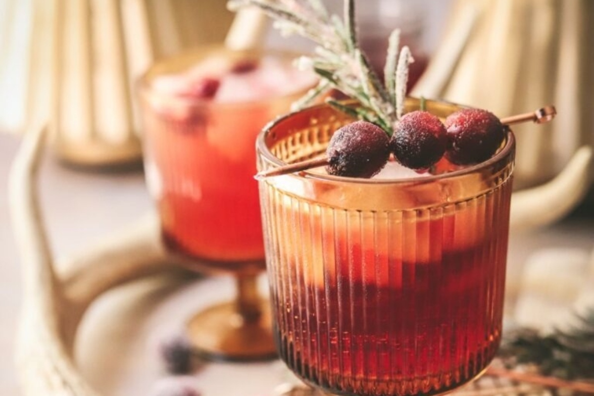 A Christmas cocktail infused with the flavors of cranberries and garnished with sprigs of rosemary.