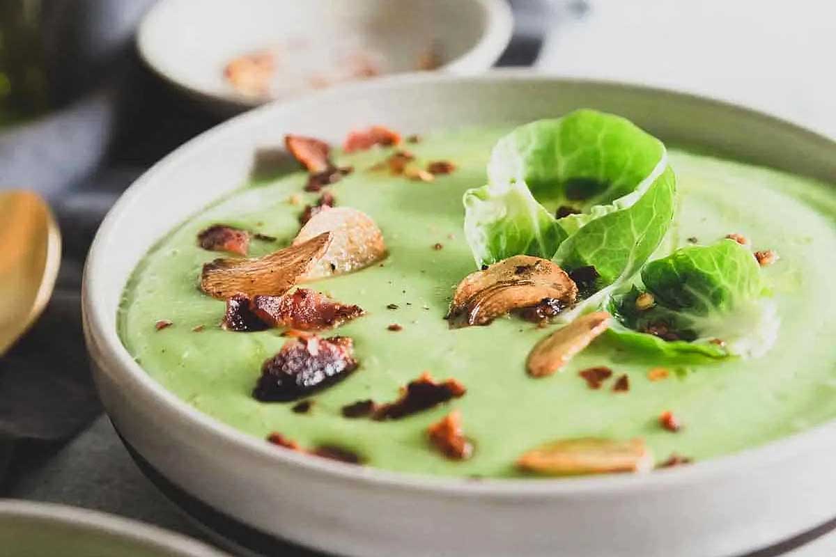 A bowl of green soup with walnuts and bacon.