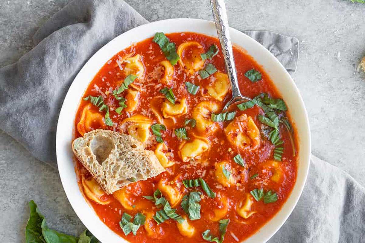 A bowl of tortellini soup with bread and basil.