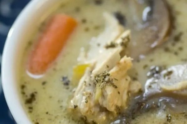 A bowl of creamy chicken soup with carrots and mushrooms.