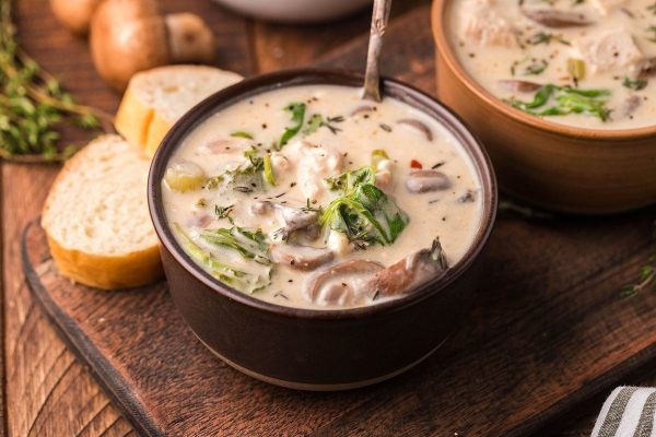 Two bowls of cream soup with mushrooms and bread on a wooden table.