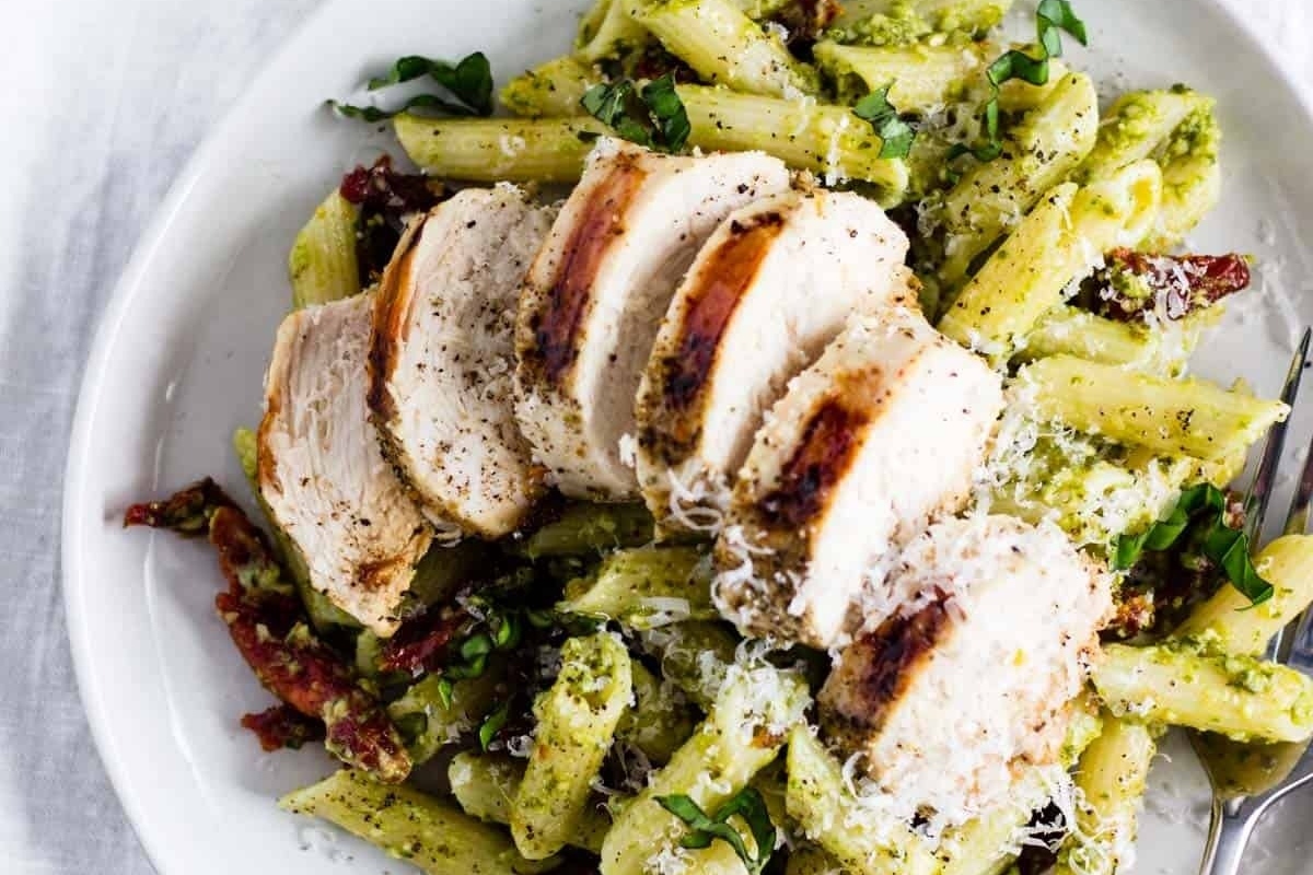 A plate of chicken and pesto pasta served on a white dish.