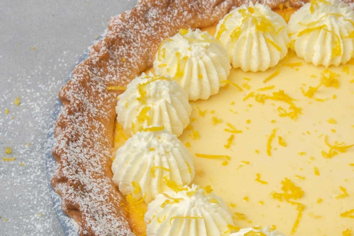 An Italian lemon tart recipe, topped with fluffy whipped cream and fresh lemon zest.
