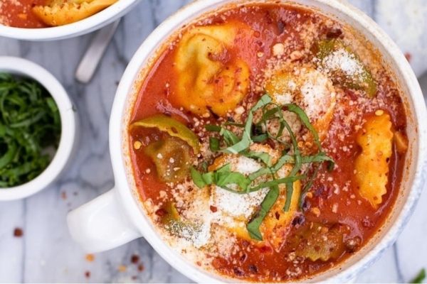 A creamy bowl of tomato soup with tortellini in it.
