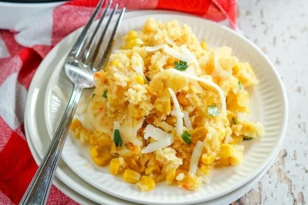 Cheesy corn casserole on a white plate with a fork.