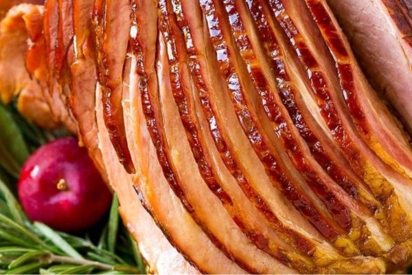 A ham is sitting on a plate with apples and cranberries.