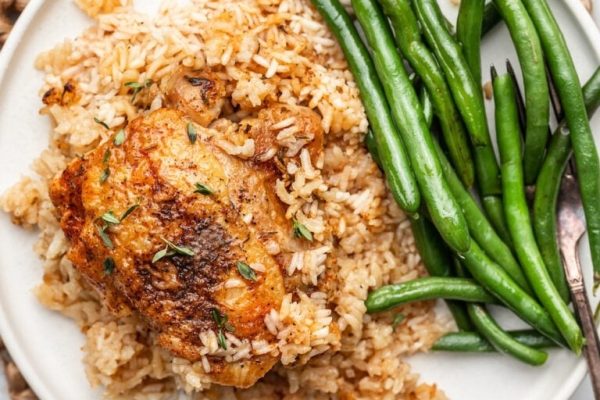 Chicken and rice on a white plate with green beans.