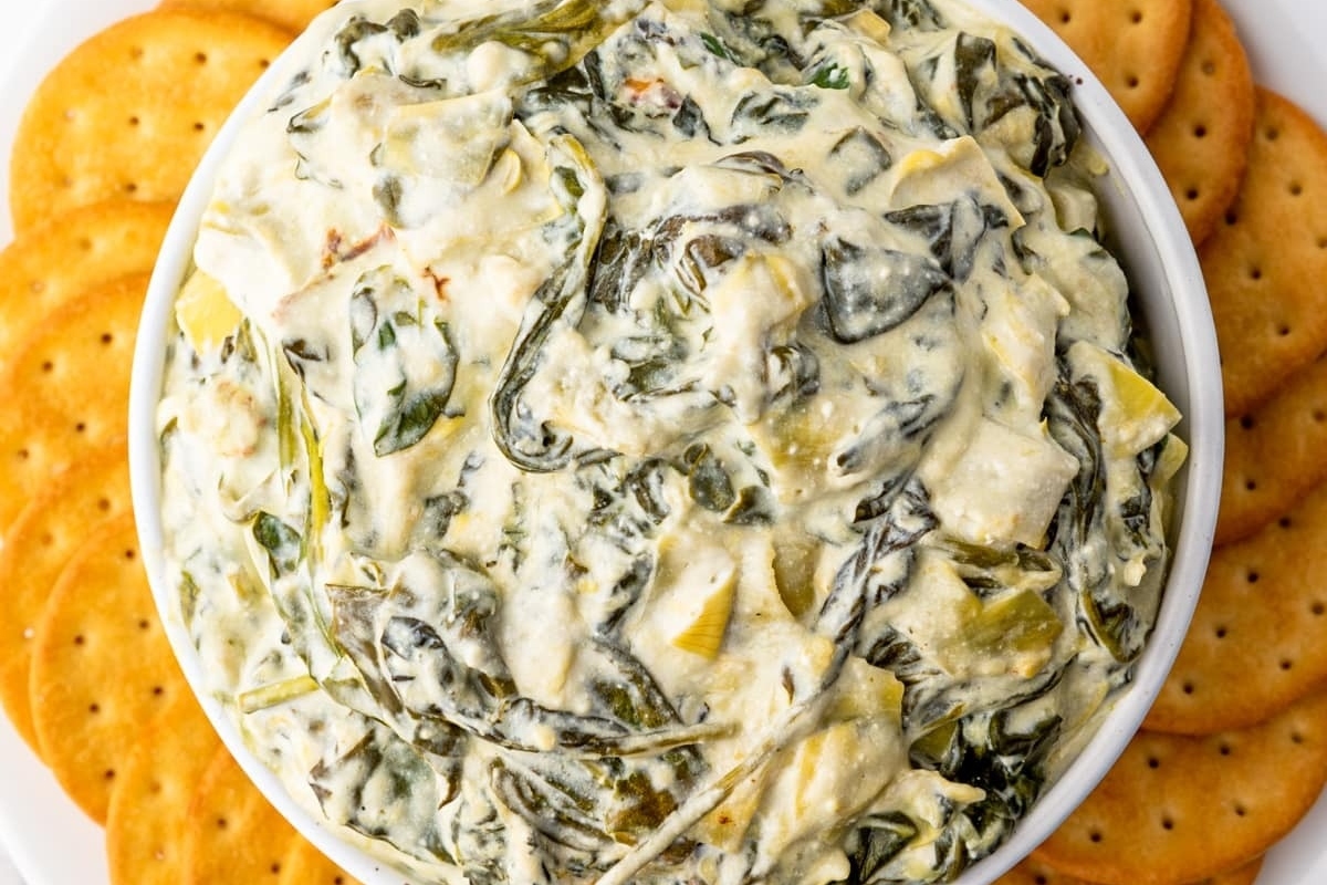 A bowl of spinach dip with crackers on top, perfect for dipping.