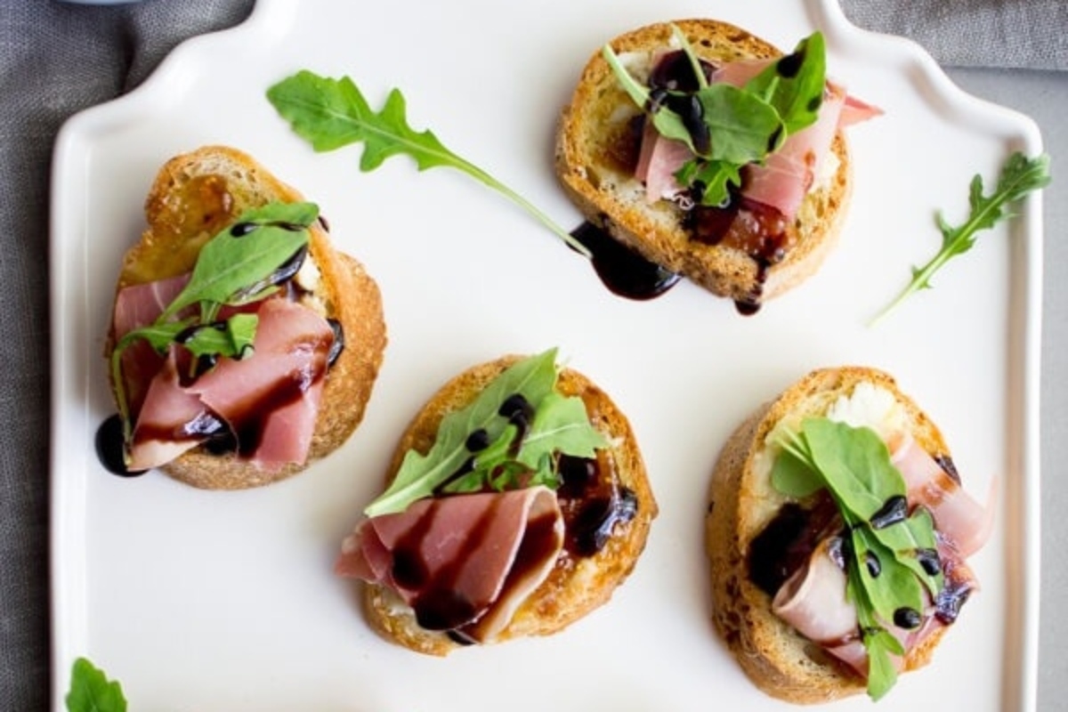 Christmas party appetizers featuring ham and arugula crostini drizzled with balsamic vinaigrette.