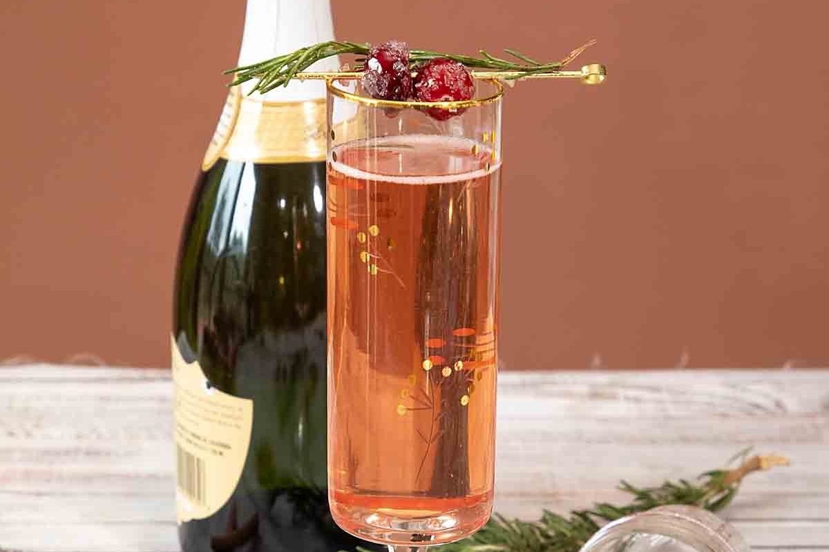 A Champagne cocktail garnished with cranberries and sprigs of rosemary.