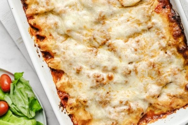 Lasagna in a white baking dish with a salad on the side.