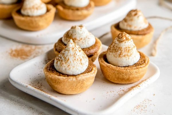 Mini pumpkin pies with whipped cream and cinnamon on a white plate.