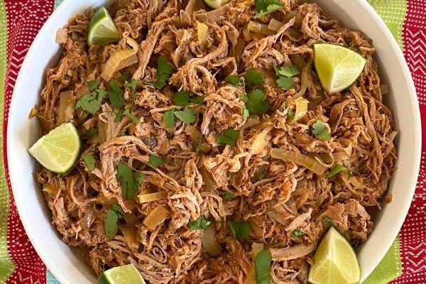 Mexican pulled pork in a white bowl with lime wedges.