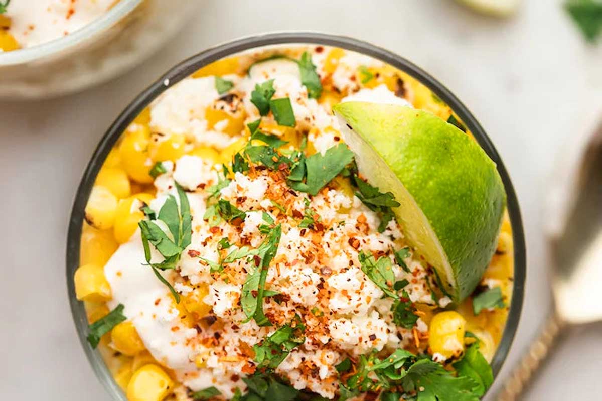 A bowl of mexican corn with lime and sour cream.