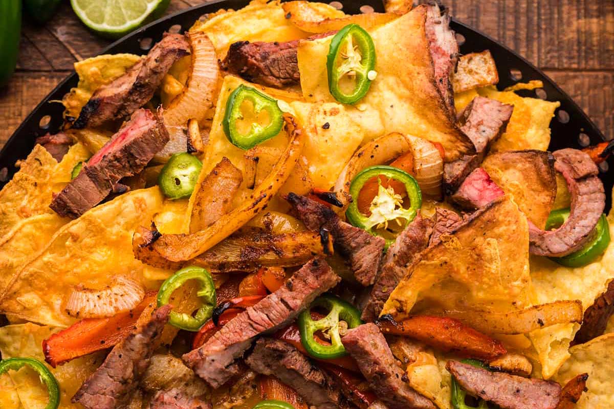 Steak nachos in a skillet on a wooden table.