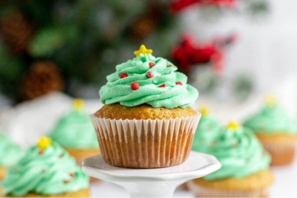 Christmas-themed cupcakes decorated with green frosting displayed on a white plate.
