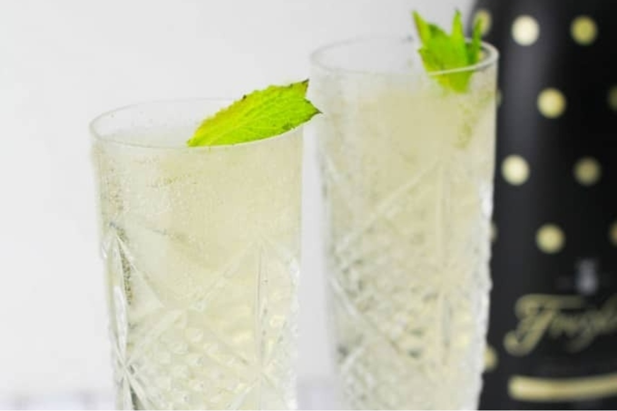 Two glasses of champagne cocktails with mint leaves and a bottle of champagne.
