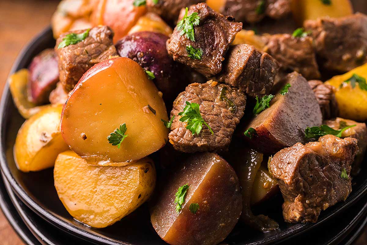 Beef and potatoes in a black bowl on a wooden table.